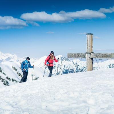 Zwei Wanderer im verschneiten Alpenpanorama nahe Gipfelkreuz unterwegs